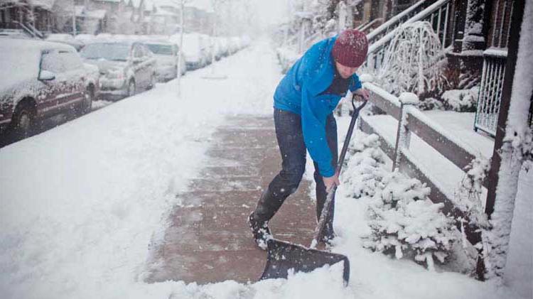 在积雪覆盖的人行道上铲雪的男子.